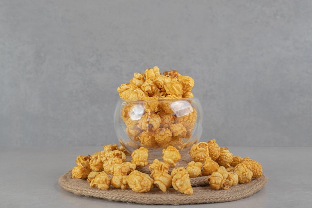 Trivet resting under a full glass bowl ringed with caramel coated popcorn on marble table.