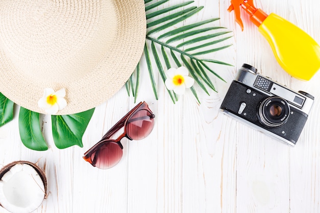 Tropical vacation arrangement with sunscreen, camera, hut, sunglasses, coconut, flowers and palm leaves