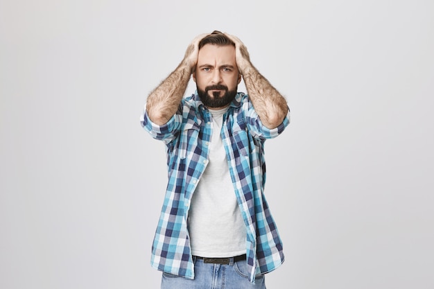 Free photo troubled bearded adult man grab head and look distressed