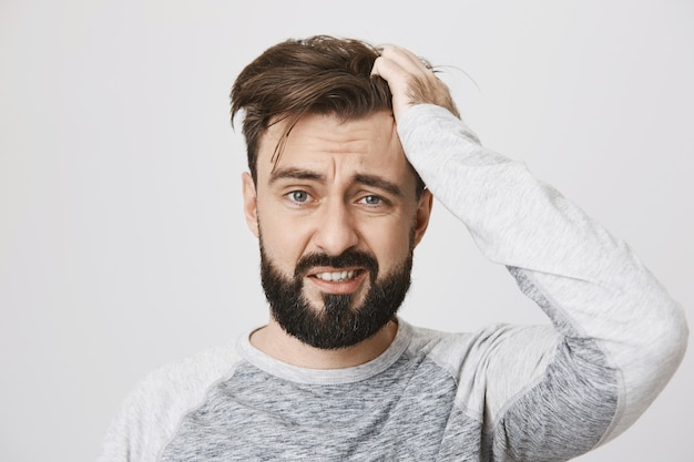 Free photo troubled bearded guy in panic tossing hair and look scared