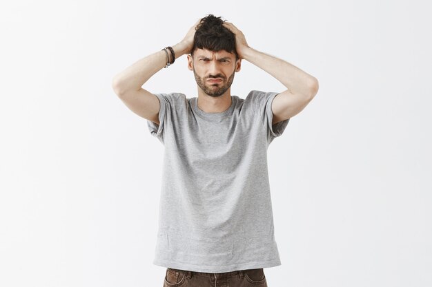 Troubled and confused handsome guy posing against the white wall