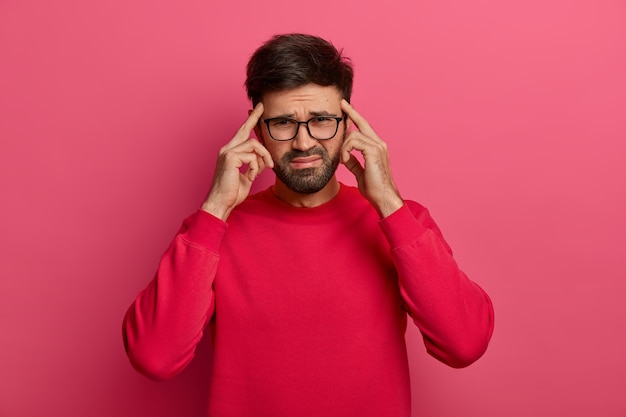 Troubled distressed bearded man keeps index fingers on temples to focuse