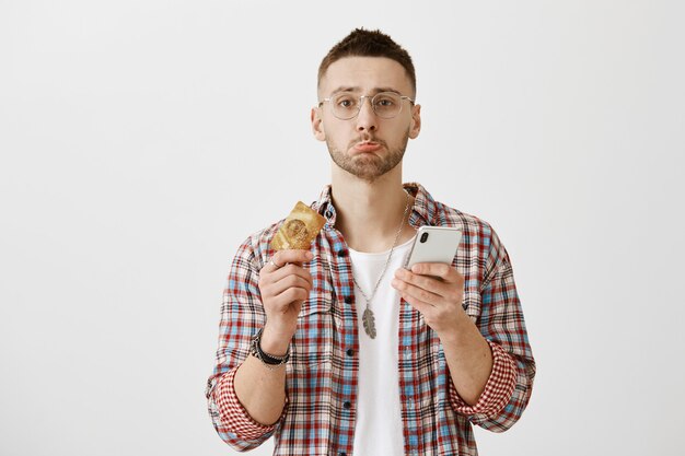 Troubled gloomy young guy with glasses posing with his phone  and card