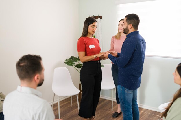 Troubled hispanic couple with marriage problems holding hands with their eyes closed and telling each other words of forgiveness during group therapy