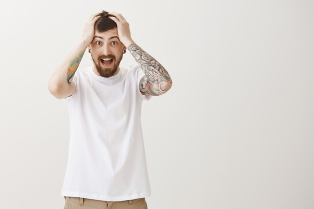 Free photo troubled tattooed guy grab head and scream in panic