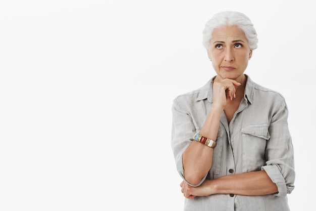 Troubled thoughtful elder woman with grey hair, looking upper left corner pondering