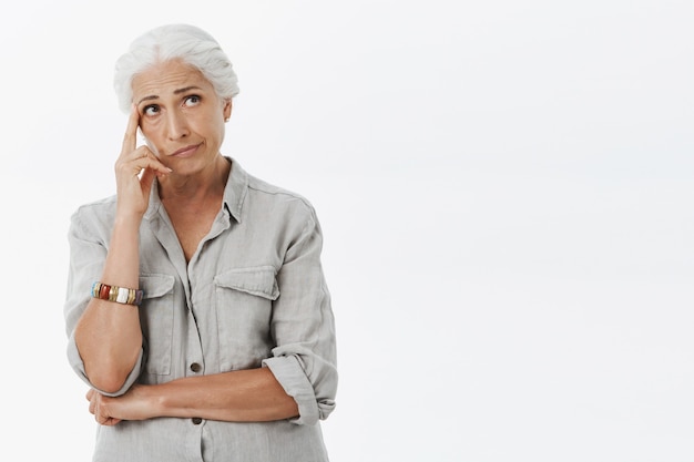 Troubled thoughtful elder woman with grey hair, looking upper right corner pondering