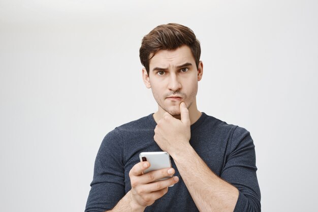 Troubled thoughtful man thinking while holding smartphone