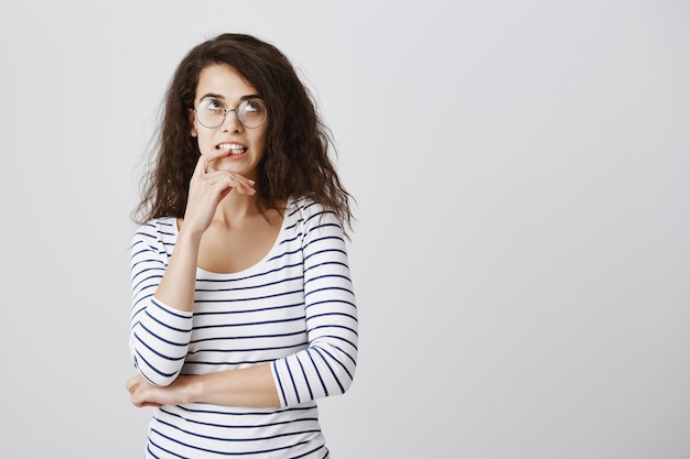 Foto gratuita donna turbata con gli occhiali morde il dito e alzando lo sguardo pensieroso, pensando