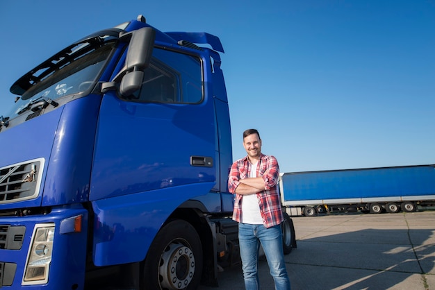 Truck driver in casual clothes standing by his truck with arms crossed at truck stop