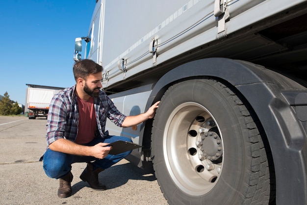 Truck driver inspecting tires and checking depth of tire tread for safe ride