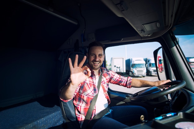 Autista di camion che ama il suo lavoro e mostra il segno di gesto giusto mentre è seduto nella sua cabina del camion