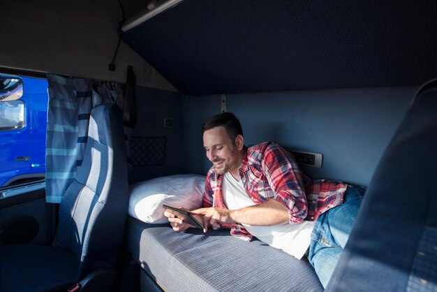 タブレットコンピューターを介して彼の家族と通信する彼のキャビンのベッドに横たわっているトラック運転手