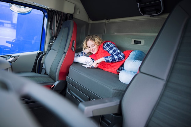 Водитель грузовика, лежа на кровати в своей кабине, общается со своей семьей через планшет