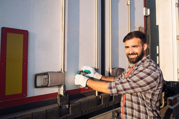 商品を降ろす準備ができているトラックトレーラーの後ろを開くトラック運転手