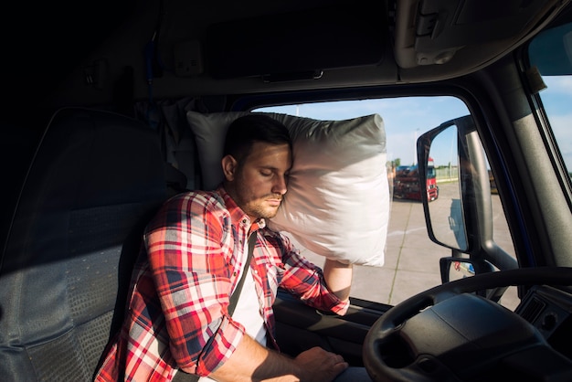 Водитель грузовика спит в кабине своего грузовика из-за езды на большие расстояния и переутомления
