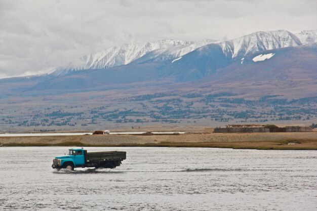 Truck driving in the river surrounded by the mountains covered in snow