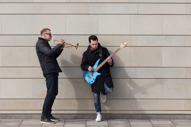 Trumpet player and guitarist playing in front of wall