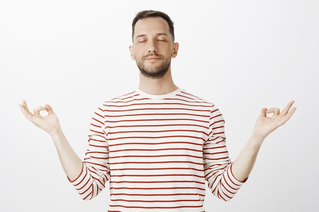 Free photo trying to find peace inside body. portrait of calm relaxed handsome husband, closing eyes and spreading hands aside with zen gesture