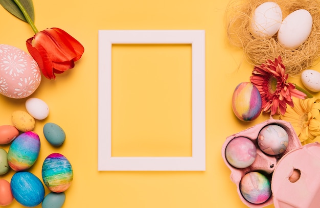 Tulip; gerbera flower; easter eggs and empty white border frame on yellow background