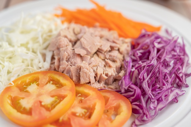 Insalata di tonno con carote, pomodori, cavolo su un piatto bianco su un pavimento di legno.