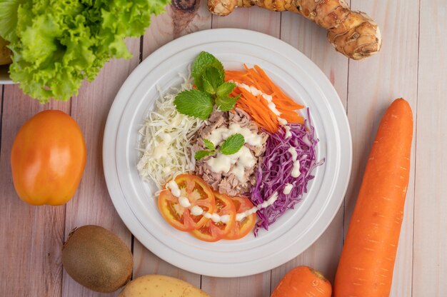 Foto gratuita insalata di tonno con carote, pomodori, cavolo su un piatto bianco su un pavimento di legno.