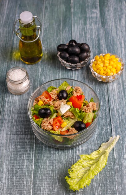 Салат из тунца с листьями салата, маслинами, кукурузой, помидорами, вид сверху