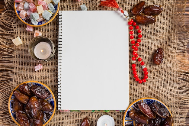 Turkish bowl of juicy dates; delight lukum with blank white page and red holy beads on jute cloth