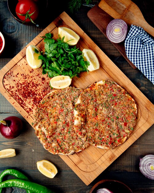 turkish lahmacun with hot peper, parsley, and lemon slices on a wooden tray