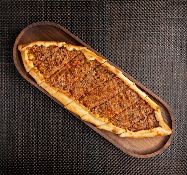 Turkish pide with stuffed meat and hot pepper on a wooden bowl