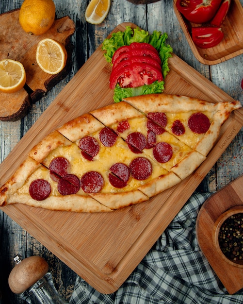 Turkish pizza pide with pepperoni , tomato and herbs.