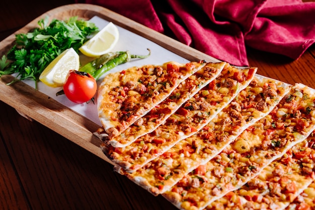 Turkish traditional lahmacun with green salad, lemon and tomato inside wooden plate.