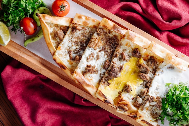 Foto gratuita lahmacun tradizionale turco con ripieno di carne e formaggio servito all'interno del piatto di legno.