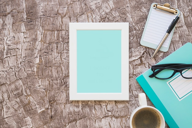 Turquoise picture frame; coffee cup; eyeglasses and clipboard with pen on background