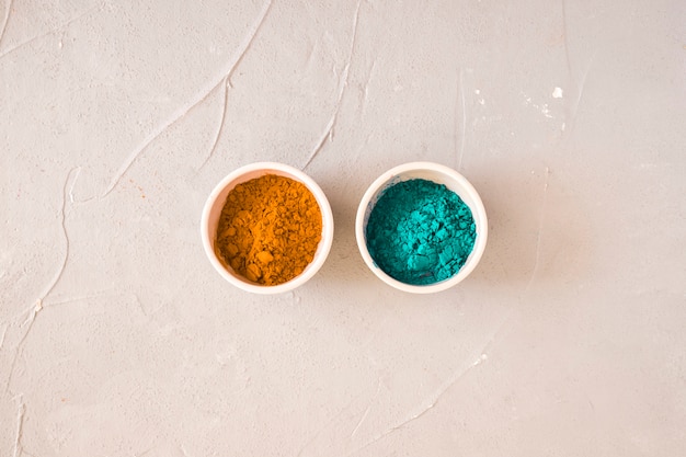 Turquoise and yellow holi color powder in the two bowl on concrete backdrop