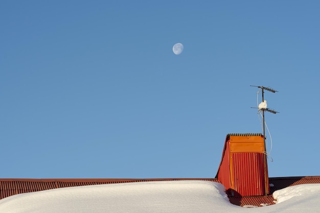 冬の降雪と青空の朝月の後の家の屋上にあるテレビアンテナ