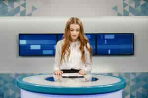 Бесплатное фото Телевидение в студии готовится к выходу в эфир. улыбающаяся девушка в белой рубашке, сидя за столом.