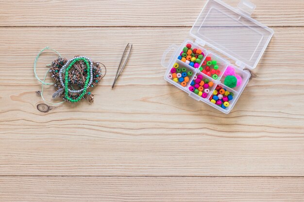 Tweezers; bracelet and beads in the white plastic box on wooden table