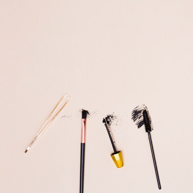 Tweezers; makeup brush; mascara brush isolated on beige background