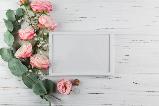 Twig; roses and baby's breath flowers near the white blank frame on wooden textured surface