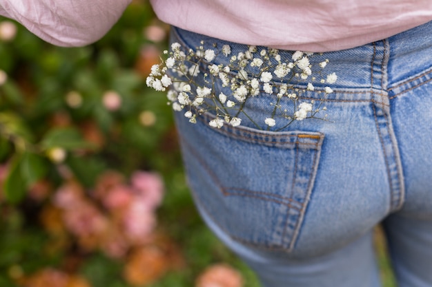 Twig with white flowers placed in back pocket of woman jeans