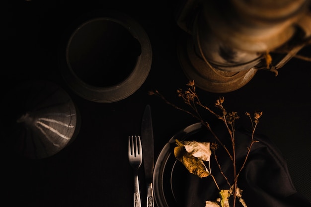 Twigs and leaves near lamp and cutlery