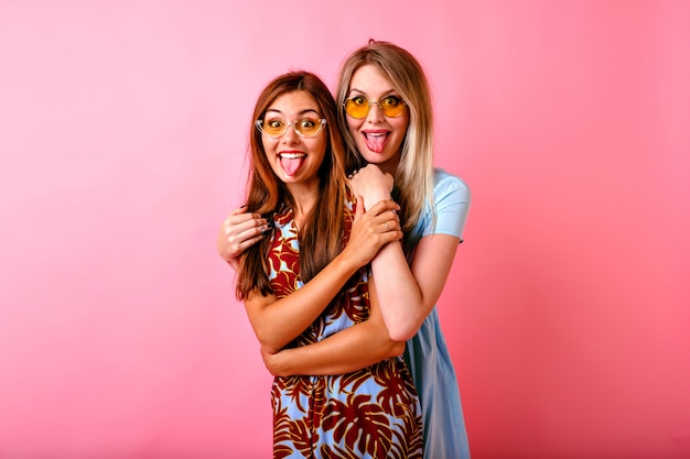 Two adorable happy young women having fun together showing tongues