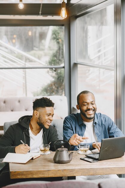 Two african-american men working behind a laptop and writing in a notebook. Men with beard sitting in a cafe.