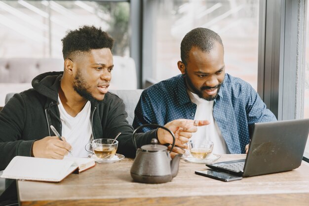 Two african-american men working behind a laptop and writing in a notebook. Men with beard sitting in a cafe.