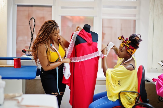 Two african dressmaker woman designed new red dress on mannequin at tailor office Black seamstress girls