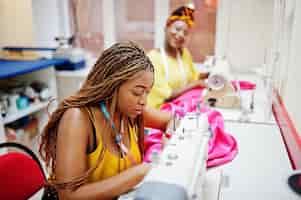 Free photo two african dressmaker woman sews clothes on sewing machine at tailor office black seamstress girls