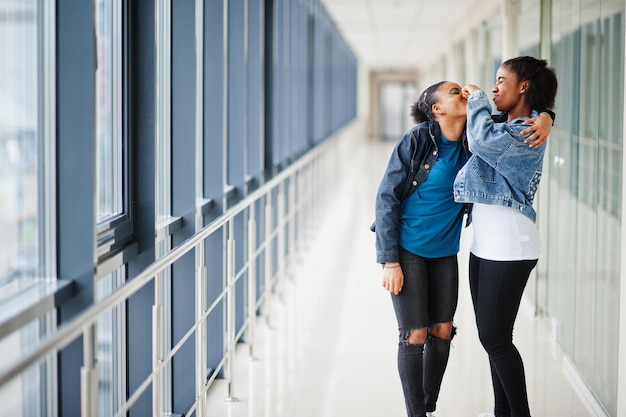 Two african woman friends in jeans jacket catch nose indoor together