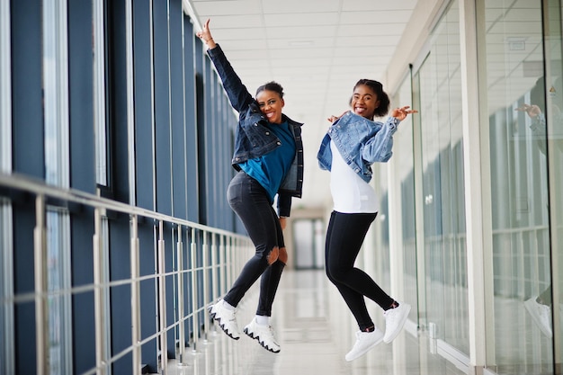 Two african woman friends in jeans jacket jumps indoor together