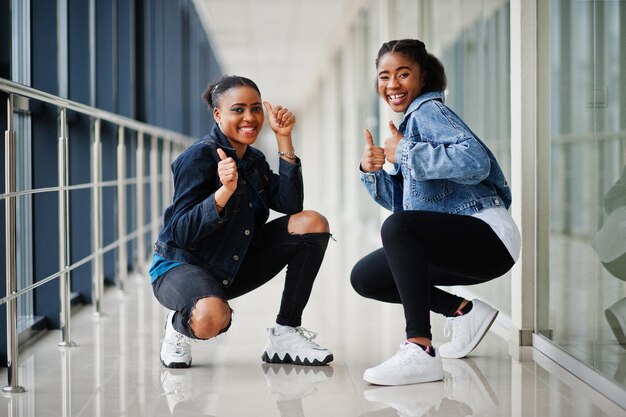 Two african woman friends in jeans jacket show thumb up indoor together